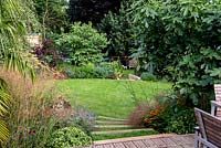 View from a wooden deck down a terraced split level garden. Planting includes Dechampsia Bronzeschlier, Echinacea Double Pink Delight 
