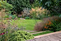 Steps planted with chamomile lead to an oval shaped lawn in a terraced split level garden. Planting includes Dechampsia Bronzeschlier, Crocosmia Solfaterre, , Stipa tenuissima. Beyond the lawn a children's play area is hidden at the back of the garden.