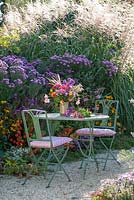 Colorful bouquet of cut flowers on table next to a mixed autumn border of asters and micanthus - ornamental grasses 