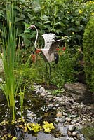 Metal bird sculpture on the edge of a pond with Typha latifolia - Common Cattails in backyard rustic garden in summer, Quebec, Canada