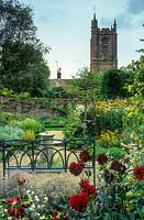 View of formal garden with blue painted wrought iron bench, old sundial, gravel paths, roses, herbaceous perennials - Cerne Abbas, Dorset