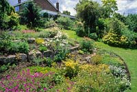 Sloping garden and lawn with view to house. Geranium psilostemon, Achillea and campanulas in border. Don and Sally Edwards, Horningsea, Cambridge