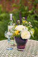 A cut flower arrangement on a garden table including Rosa 'Patience'