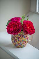 A cut flower arrangement of roses in a patterned jug on a windowsill