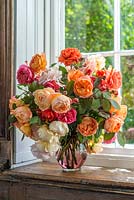 Orange, pink, peach and white roses in a cut flower arrangement on a windowsill