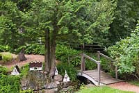 Wooden footbridge and wood and metal birdhouses underneath a white Cedrus - Cedar tree in front yard country garden in summer, Quebec, Canada