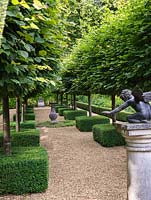In secret, sunken formal garden, avenue of pleached limes, with their trunks encased in box squares. On pedestal, statue of Cupid. Central sundial.