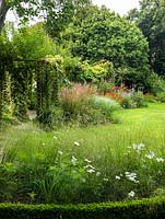 A view through box edged beds planted with Deschampsia 'Bronzeschleier' and white Cosmos. Behind is a wooden pergola and late summer border planted with Echinops 'Nivalis', Crocosmia 'Lucifer' and Helenium 'Moorheim Beauty'.