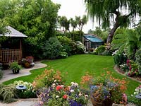 A town garden with a lawn, covered seating area, greenhouse and annual containers.