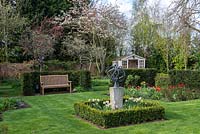 A formal grass parterre surrounded by yew - Taxus hedging. An Armillary sphere is set in boxed edged bed with Narcissus, the bed behind is planted with Tulips and roses. At the far end Amelanchier and Malus trees are in blossom.