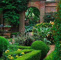 View over box parterre filled with Salvia patens 'Cambridge Blue' and Dahlia 'Gallery Cezanne', Galactites tomentosa, lilies and argyranthemum. Brick arch leads to South Lawn.