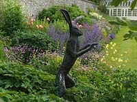 Hare sculpture in herbaceous border amidst glorious muddle of Sisyrinchium striatum, eryngium, Alchemilla mollis, hardy geranium, Aquilegia vulgaris, catmin, rose.
