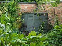 Tiny kitchen plot at rear of 30m x 8m cottage garden. Compost heap built from reclaimed timber, and painted 'Wild Thyme' blue. Seen over bed of courgette, sweetcorn and leeks.