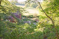 View of C16 house and countryside beyond from top of steep woodland garden through trees