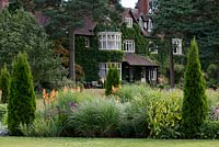 A view of Abbeywood House, an Edwardian residence built in 1908, seen  accross a herbaceous border of perennials, grasses and repeated coonifers.