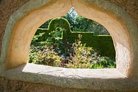 Metal water feature designed and made by Michael Chaikin viewed through a window in the cob wall. Garden planted with rodgersias, witch hazels, roses and amsonia. Caervallack Farm, St Martin, Helston, Cornwall, UK