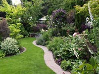 A shaped grass path leads through mature mixed borders. A small stone bench provides the focal point.