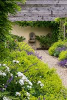 A gravel path leading to a water feature lined by Alchemilla mollis and Nepeta 'Six Hills Giant' beneath a wooden pergola.