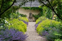 A gravel path leading to a water feature lined by Alchemilla mollis and Nepeta 'Six Hills Giant' beneath a wooden pergola.
