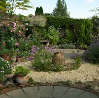 A circular themed gravel garden and patio with cottage garden style planting. Armeria Joystick and a terracotta urn provide a focal point in the centre of the gravel bed