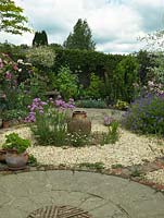 A circular themed gravel garden and patio with cottage garden style planting. Armeria Joystick and a terracotta urn provide a focal point in the centre of the gravel bed.