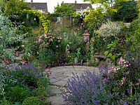 A small circular patio in the middle of a gravel garden. Privacy is created by the surrounding planting which includes Rosa Mundi, Nepeta Six Hills Giant, Geranium Nimbus, Buxus sempervirens and Stipa gigantea.