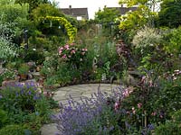 A small circular patio in the middle of a gravel garden. Privacy is created by the surrounding planting which includes Rosa Mundi, Nepeta Six Hills Giant, Geranium Nimbus, Buxus sempervirens and Stipa gigantea.