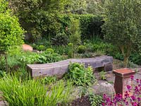 Herb and gravel garden with a central sinuous wooden bench crafted by Anthony Paul. Planted with rosemary, fennel, angelica, sweet cicely, bay tree, acanthus and geum.