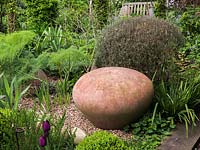 Dome shaped terracotta seat next to rosemary bush in gravel garden with epimedium, fennel and tulips.