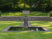 Water tumbles from a spout, along a rill set into a lawn, and into a silent pool that reflects the sky and nearby trees.