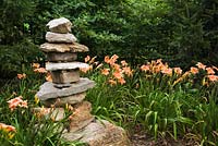 Stacked rock sculpture and orange Hemerocallis 'Strawberry Candy' in the Route des Gerbes d'Angelica garden, Mirabel, Quebec, Laurentians, Canada