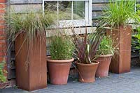 Terracotta and rusted steel containers planted with Phormium tenax, Deschampsia flexuosa and pennisetum ornamental  grasses.
