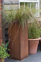 A tall rusted steel container overflows with ornamental grass Deschampsia flexuosa.