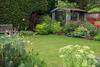 A small lawn creates a calm, green space between the busy, overflowing borders.