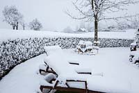 Winter aspect with snow covered garden furniture, a hedge and the view to the landscape, Cornus mas