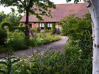 View of house along the gravel driveway, through foxglove, hardy geranium and astrantia.