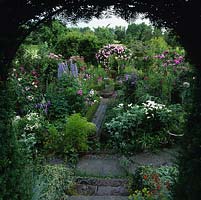 Yew arch leads to box parterre and sundial surrounded by beds of roses, Delphinium 'Alice Artindale', clematis, eryngium, lilies, pinks, scabious, aconitum, campanula and phlox.