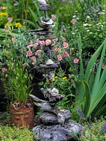 Driftwood sculpture totem poles set against a bed of summer perennials. Unusual head-shaped plant pot filled with quaking grass.