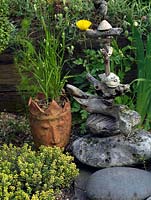 Driftwood sculpture totem poles set against a bed of summer perennials. Unusual head-shaped plant pot filled with quaking grass.