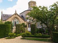 An unusually shaped parterre, using box hedges, yew and imposing cylindrical shapes clipped from Portuguese laurel, flanks the entrance to a former Victorian schoolhouse.