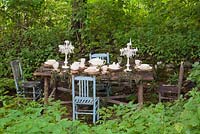 Wooden dining table and chairs set up in the Shade Garden in the La Seigneurie de L'Ile d'Orleans private estate garden in summer, Saint-Francois, Ile d'Orleans, Quebec, Canada