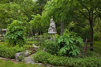 Grey cement birdhouse sculpture and borders planted with Ricinus communis - Castor Bean plants in private backyard formal garden in early summer
