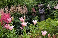 Lilium and Astilbe flowers with statue of a religious monk in border 