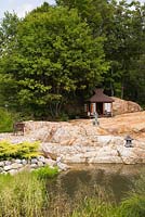 Rock formed pond with Japanese tea salon, sculptures, Juniperus - Juniper shrubs and deciduous trees in private front yard Zen garden in summer