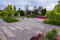 General view of the garden with gravel and brick surfaces. Dark red bench gives a contrast in general monochromatic set of plant colors