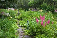 Flagstone path and borders with mauve Astilbe 'False spirea', yellow Hemerocallis - Daylily flowers and statuettes in private backyard garden in summer