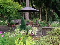 Seen over Nicotiana sylvestris and cosmos, stone terrace with table, chairs and benches. Pots of lilies, marguerites and box cones. Arch of star jasmine. 