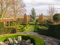 View down formal French garden, enclosed in hornbeam with circular pool and fountain, upright hornbeams, yew topiary towers and parterres of gold and dark box hedges.