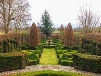 View down formal French garden, enclosed in hornbeam with circular pool and fountain, upright hornbeams, yew topiary towers and parterres of gold and dark box hedges.