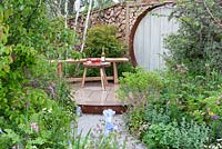 Rustic wooden bench, circular gateway and split log wall beyond, 'Shears and Chardonnay', show garden, RHS Malvern Spring Festival 2014